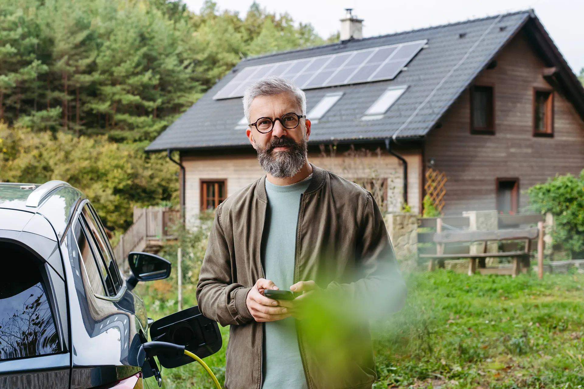 Eigentümer vor seinem Haus mit Solardach und geladenem Elektroauto